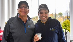 Two men dressed for golf smile at the camera while holding a candle