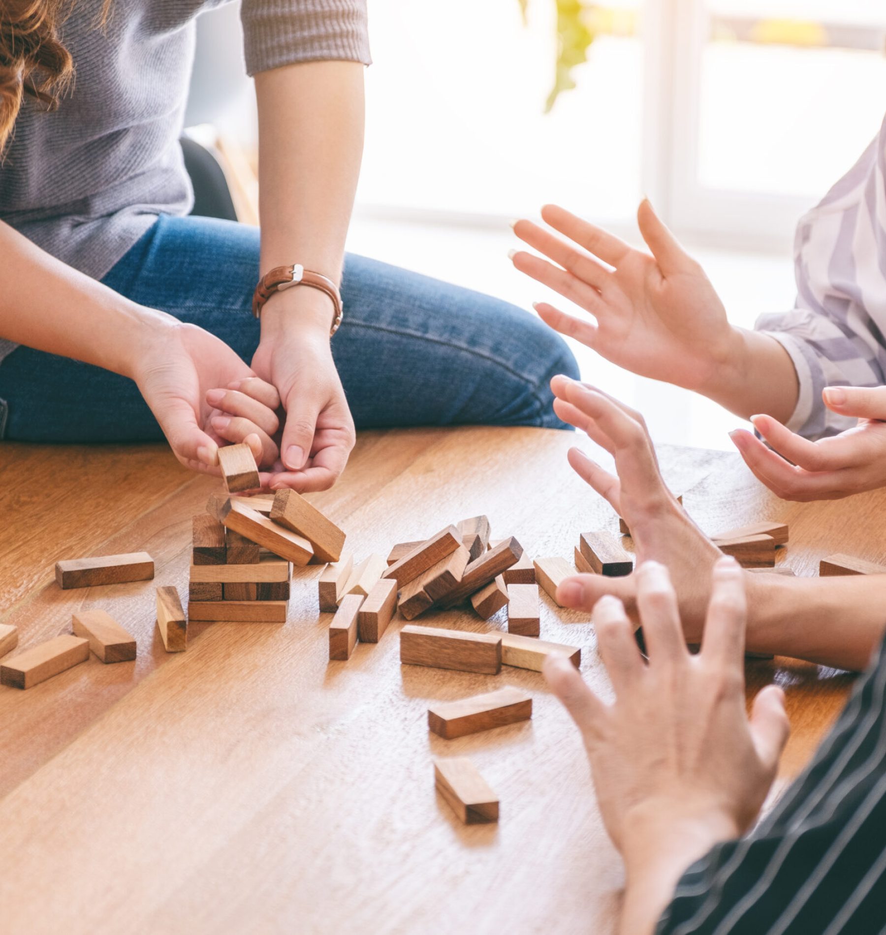 Group of friends sitting and playing Tumble tower wooden block game together with feeling happy